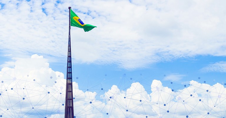 Céu azul com nuvens e bandeira brasileira em mastro alto e conectores de tecnologia na base