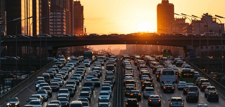 Imagem panorâmica de uma avenida da cidade de São Paulo com diversos carros e um pôr do sol