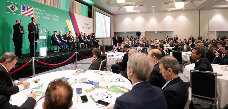 Presidente Bolsonaro discursa em auditório cheio, observado pelo presidente do Serpro, Caio Mario Paes de Andrade, à direita da foto.
