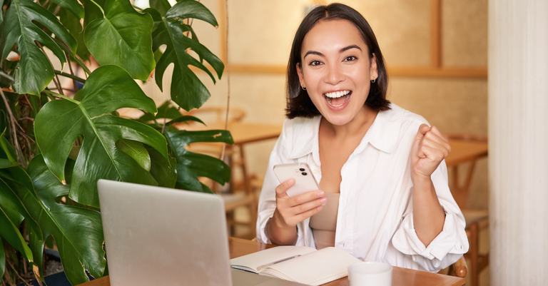 Foto de uma jovem alegre comemorando boas notícias recebidas no celular